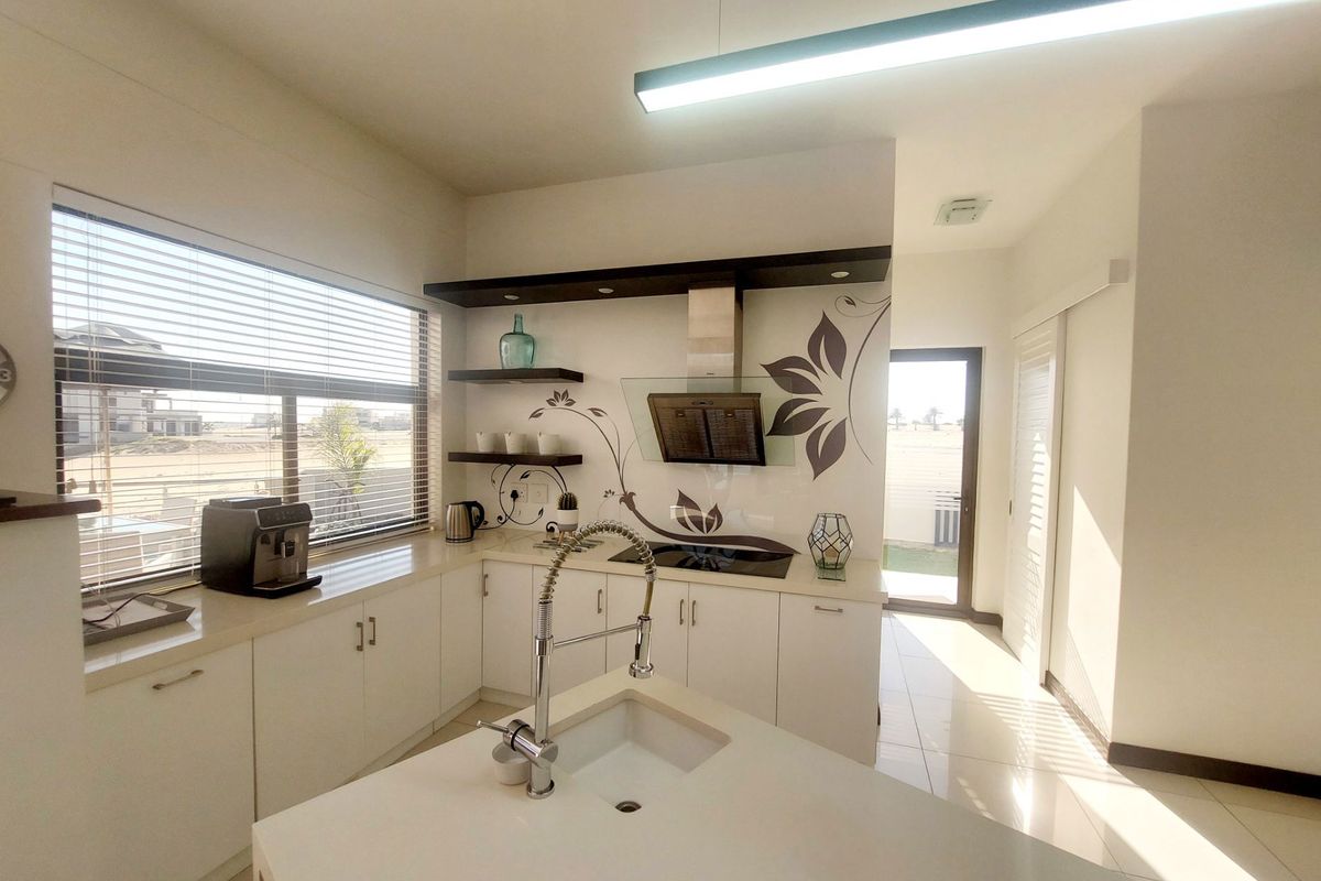 Modern kitchen featuring a central island with an undermount sink, quartz countertops, built-in hob, extractor fan, and sleek white cabinetry with floating shelving.