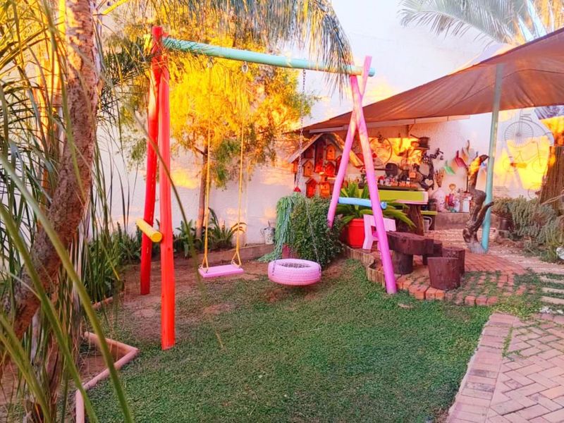 A backyard garden area featuring a lawn, brick paved pathway, and a shade sail structure.
