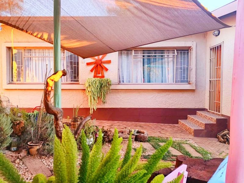 A rear patio area featuring a shade sail, paved flooring, and security features on the windows and entrance.