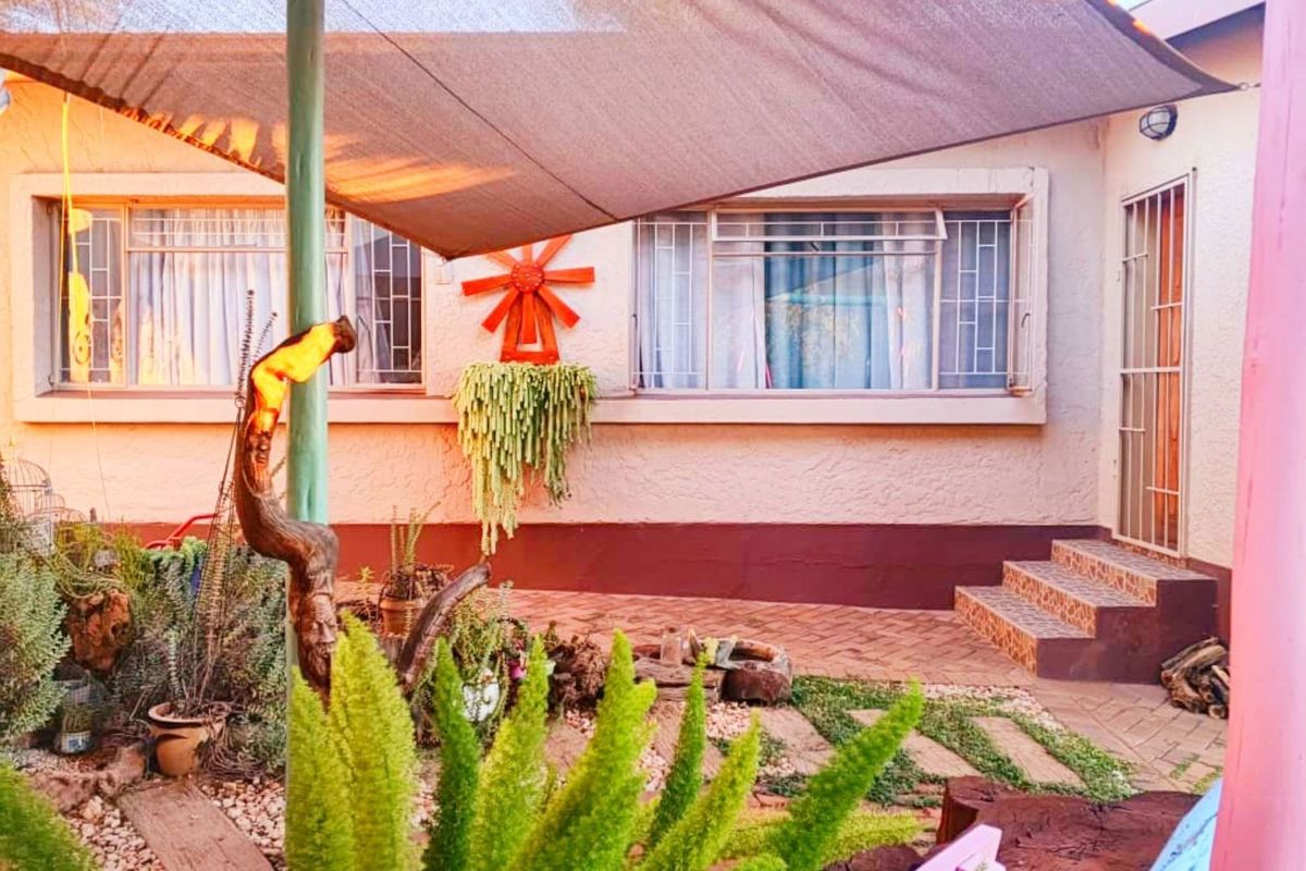 A rear patio area featuring a shade sail, paved flooring, and security features on the windows and entrance.