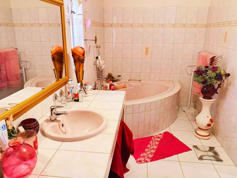 A dated bathroom featuring a corner bathtub, tiled vanity with integrated sink, and full-height wall tiling.