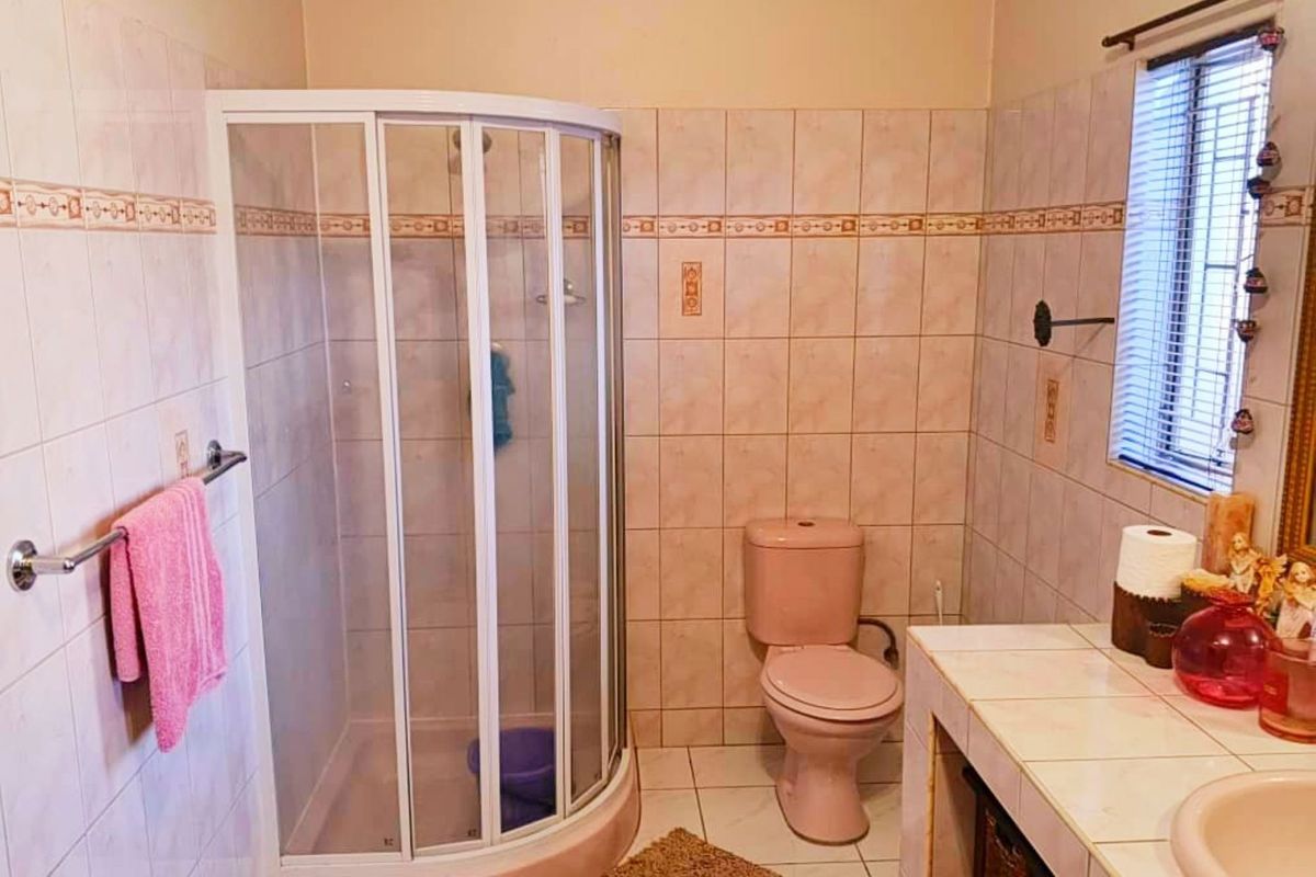 A functional bathroom featuring a corner shower enclosure, tiled vanity with integrated sink, and a toilet, finished with dated wall tiles.