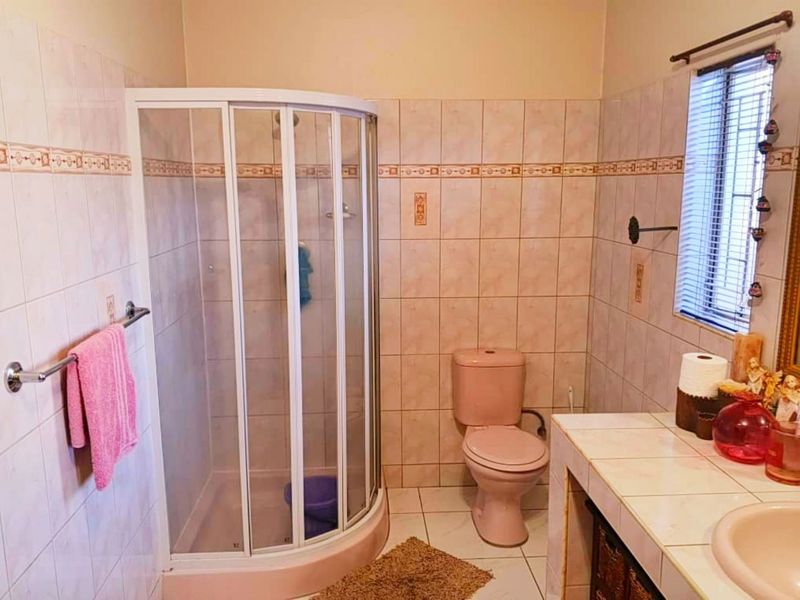 A functional bathroom featuring a corner shower enclosure, tiled vanity with integrated sink, and a toilet, finished with dated wall tiles.
