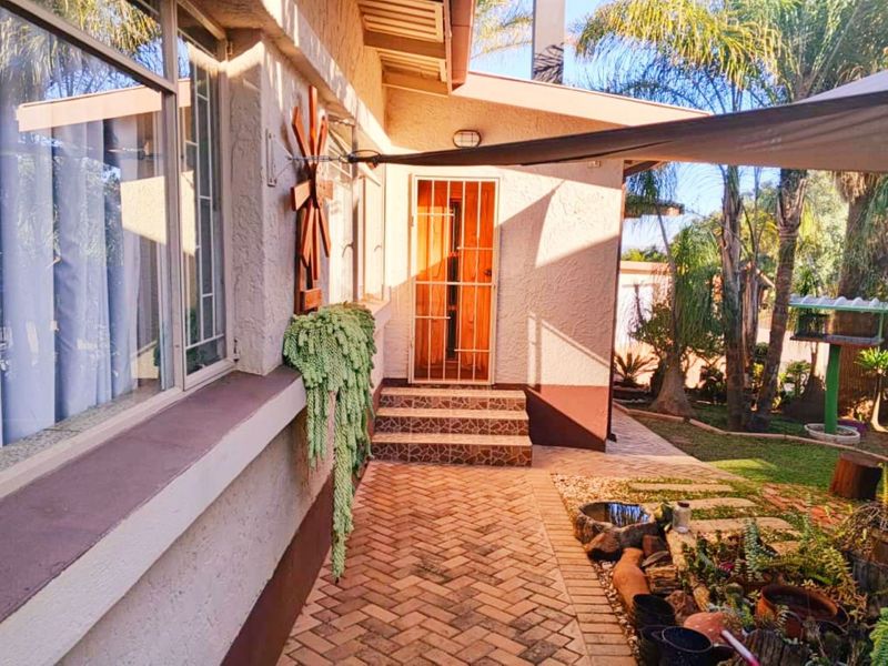 Rear exterior view featuring a brick paved walkway, tiled steps leading to a security gate, and a shade sail over the patio area.