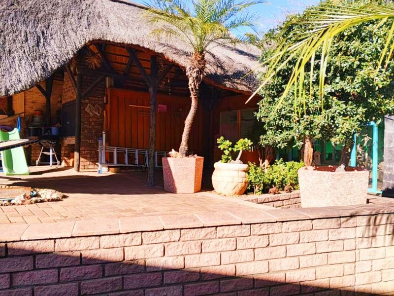 A covered outdoor patio area featuring a traditional thatched roof, brick walling, and a built-in braai, perfect for outdoor entertaining.
