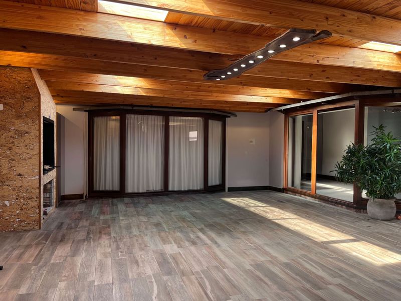 Spacious living area featuring exposed timber ceiling beams, skylights, wood-look tile flooring, and a built-in fireplace, opening to an adjacent space via sliding glass doors.