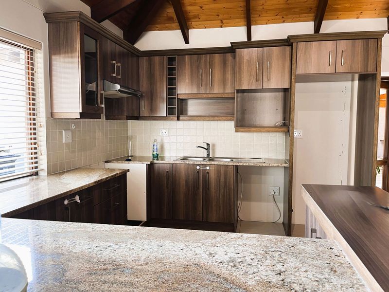 A well-maintained kitchen featuring granite countertops, dark wood-look cabinetry, tiled backsplash, and exposed timber ceiling beams, offering a functional and classic aesthetic.