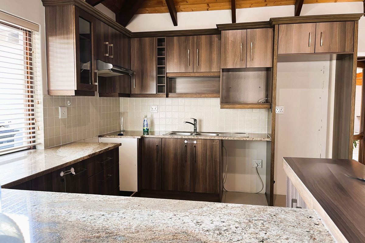 A well-maintained kitchen featuring granite countertops, dark wood-look cabinetry, tiled backsplash, and exposed timber ceiling beams, offering a functional and classic aesthetic.