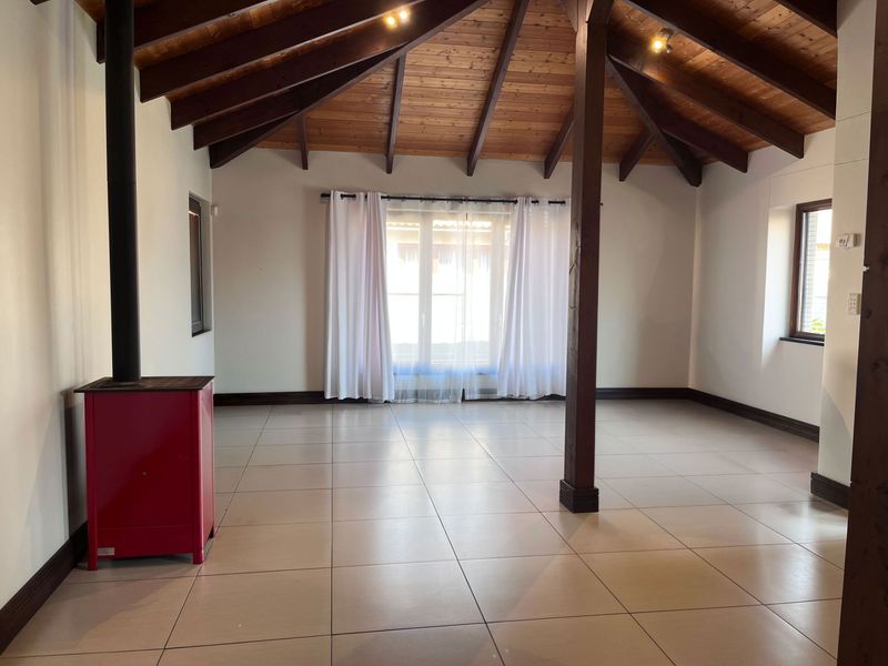 Spacious living area featuring a vaulted timber ceiling with exposed beams, ceramic tiled flooring, and a prominent freestanding wood-burning stove.