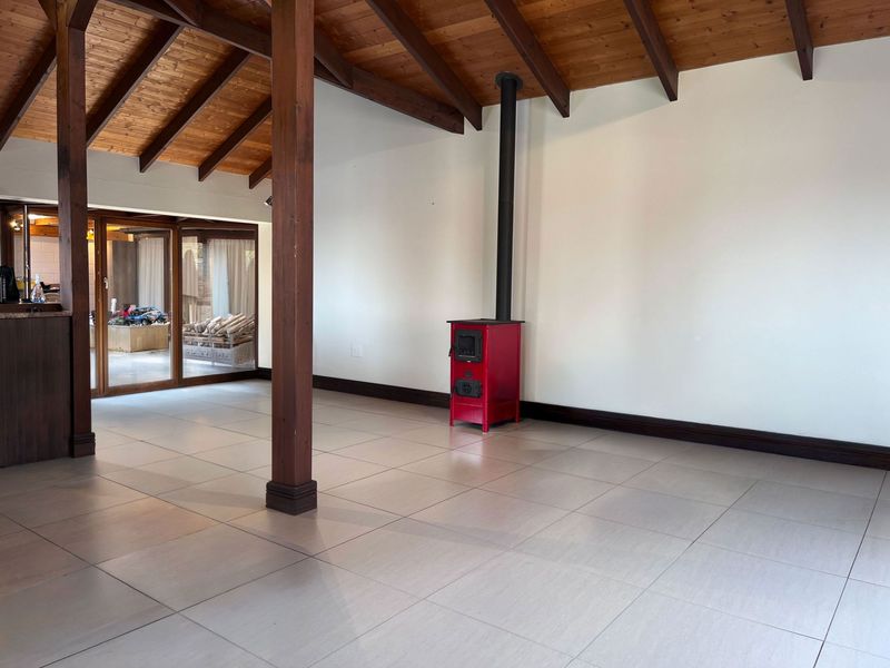 Spacious living area featuring exposed timber ceiling beams, large format floor tiles, and a prominent red freestanding wood-burning fireplace.
