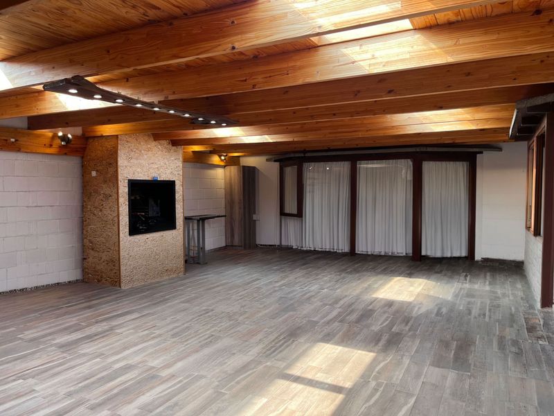 Spacious living area featuring exposed timber beam ceilings with integrated skylights, tiled flooring, and a central built-in fireplace.