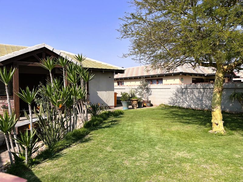 A well-maintained rear garden featuring a lush lawn, mature tree, and a covered patio area with timber decking and brick boundary walls.