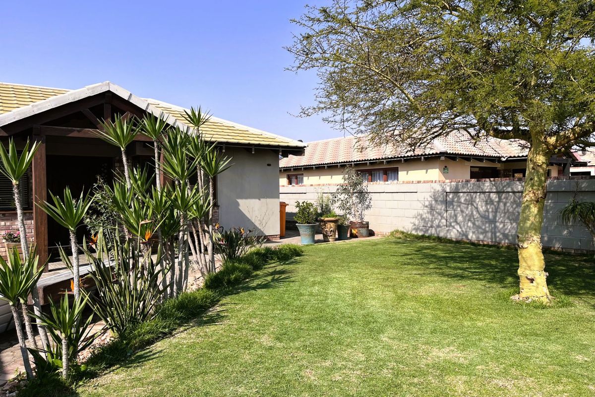 A well-maintained rear garden featuring a lush lawn, mature tree, and a covered patio area with timber decking and brick boundary walls.