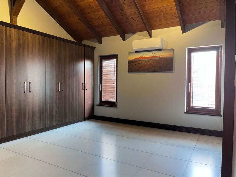 Spacious bedroom featuring high vaulted ceilings with exposed timber rafters, built-in cupboards, tiled flooring, and a wall-mounted air conditioning unit.