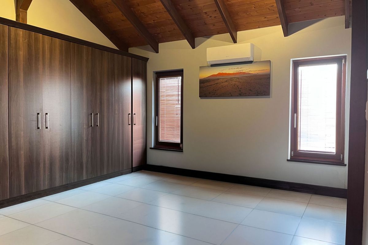 Spacious bedroom featuring high vaulted ceilings with exposed timber rafters, built-in cupboards, tiled flooring, and a wall-mounted air conditioning unit.