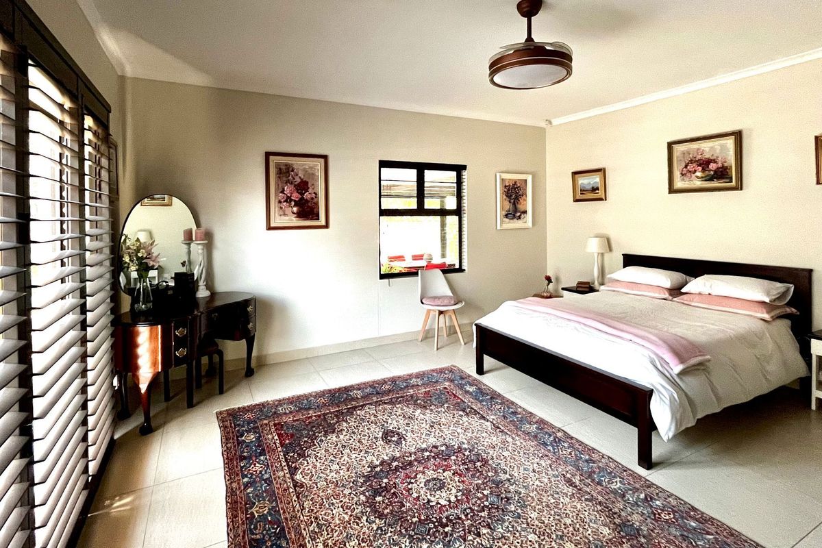 A well-maintained bedroom featuring tiled flooring, a ceiling fan, and plantation shutters, offering a bright and comfortable living space.