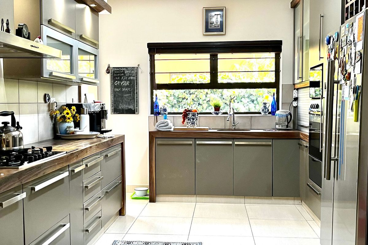 Modern kitchen featuring sleek grey cabinetry, warm wooden countertops, integrated appliances, and large windows providing ample natural light.