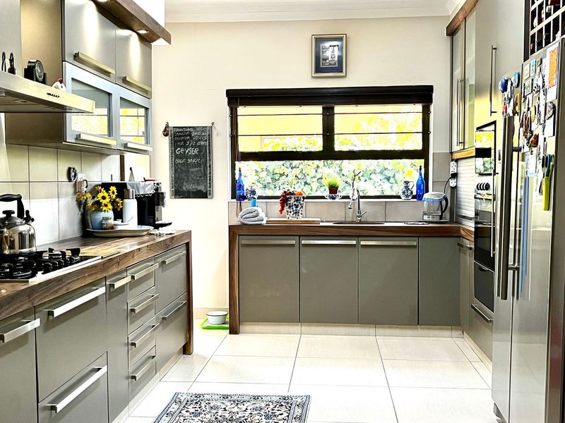 Modern kitchen featuring sleek grey cabinetry, warm wooden countertops, integrated appliances, and large windows providing ample natural light.