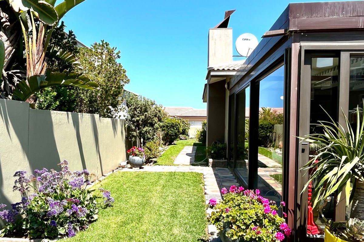 A well-maintained rear garden featuring a manicured lawn, paved pathway, boundary wall, and large sliding glass doors leading into the home.