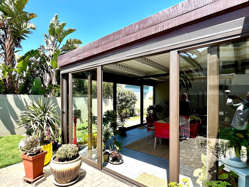 A covered patio area featuring large sliding glass doors, paved flooring, and direct access to the garden.