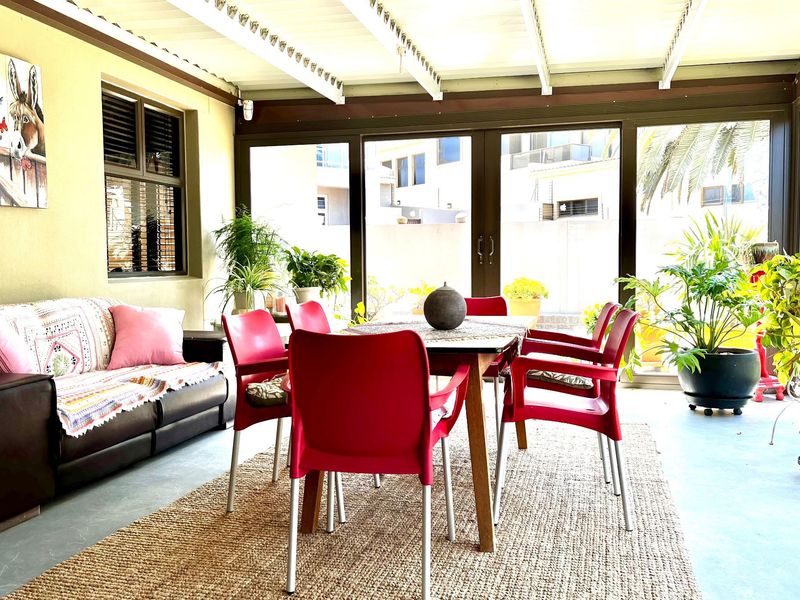 A bright, covered patio area featuring large sliding glass doors, exposed beam ceiling, and ample space for outdoor dining and relaxation.