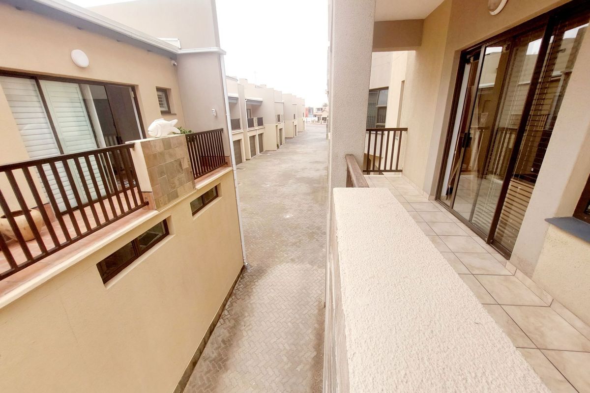 View from an upper-level balcony overlooking a paved complex driveway and adjacent apartment building facades.