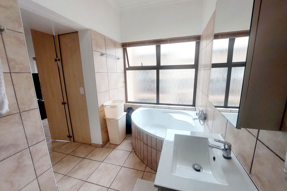 A functional bathroom featuring a corner bathtub, vanity basin, and neutral wall and floor tiling, providing a clean and practical space.