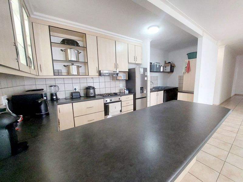 Open plan kitchen featuring light wood cabinetry, dark countertops, built-in oven, gas hob, and a breakfast bar, flowing into a tiled utility area.