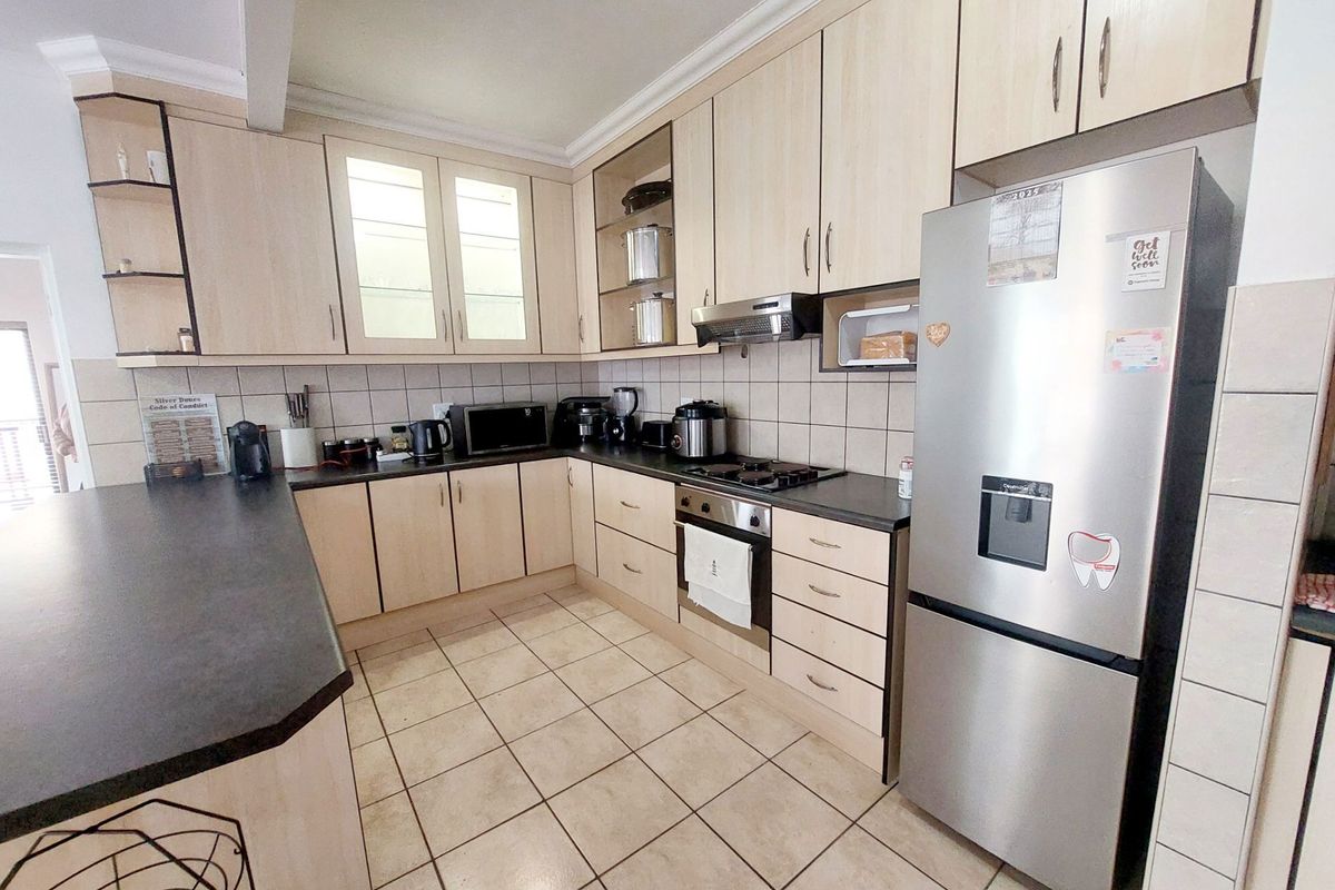 A functional kitchen featuring light wood-tone cabinetry, dark countertops, ceramic tile flooring, and integrated cooking appliances with a breakfast bar area.