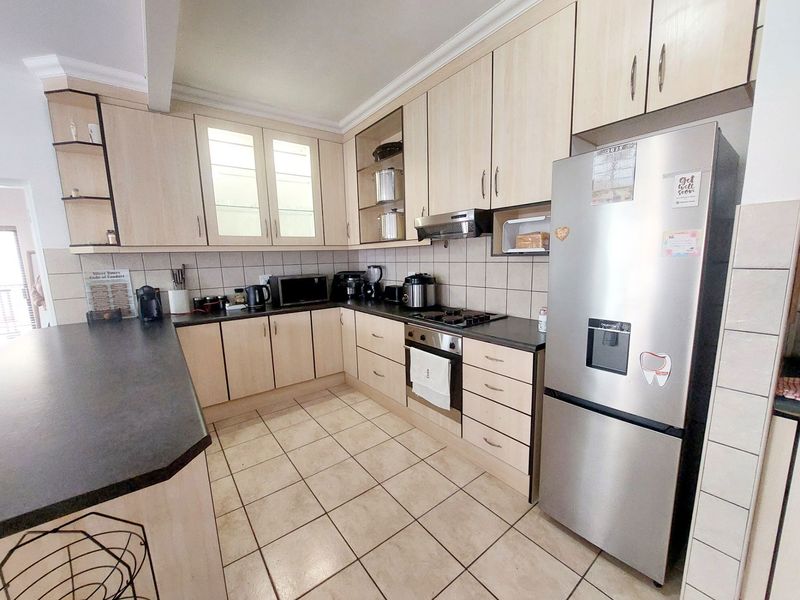 A functional kitchen featuring light wood-tone cabinetry, dark countertops, ceramic tile flooring, and integrated cooking appliances with a breakfast bar area.