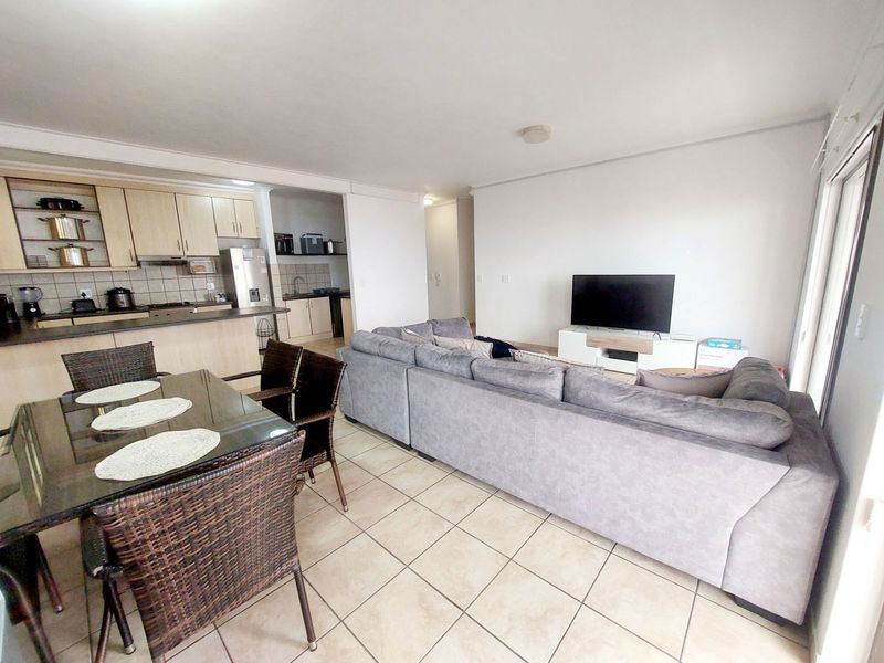 Open-plan living area featuring a tiled floor, dining space, and a functional kitchen with built-in cabinetry and integrated appliances.