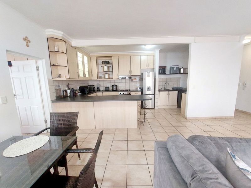 Open-plan kitchen featuring light wood cabinetry, laminate countertops, and tiled flooring, seamlessly connected to the living and dining area.