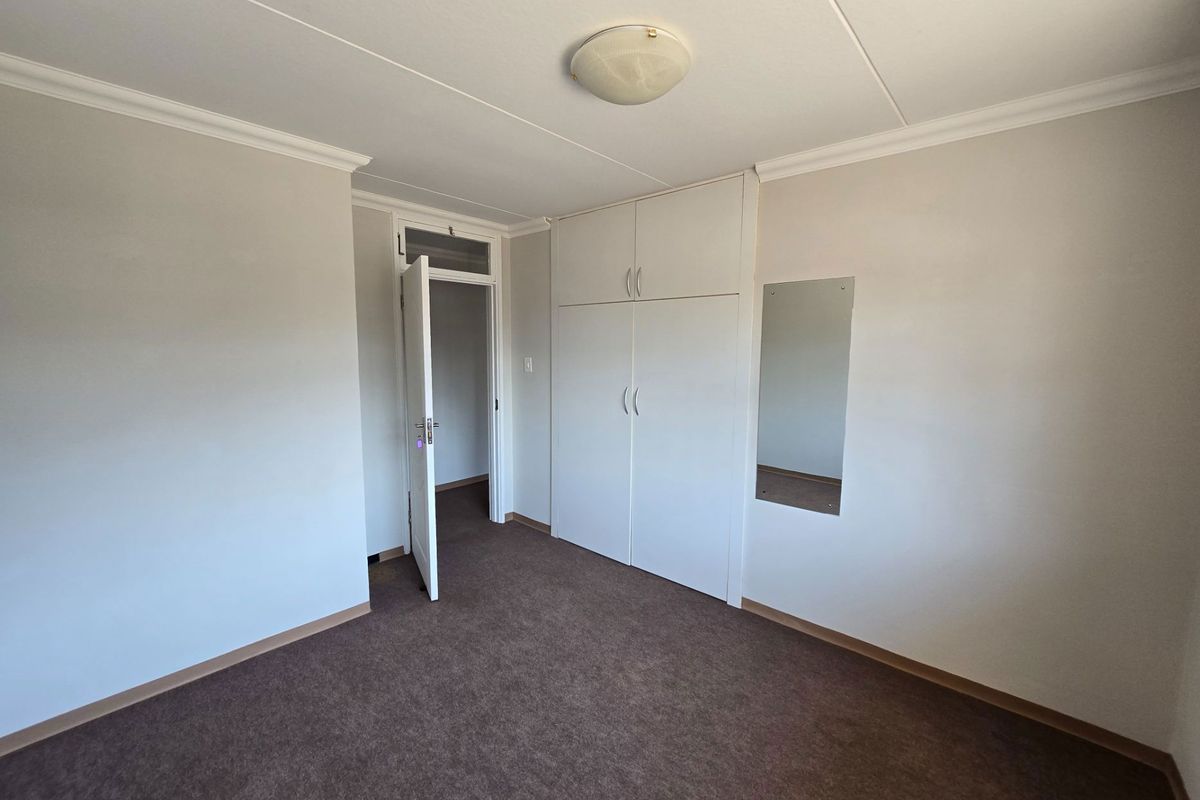 A clean, empty bedroom featuring neutral walls, carpeted flooring, and built-in storage cupboards with a flush mount ceiling light.