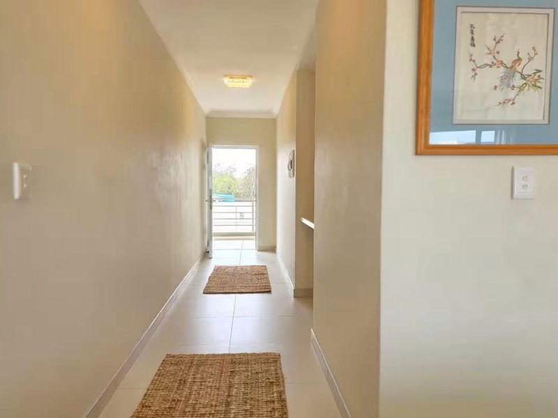 A bright, neutral-toned hallway featuring tiled flooring and recessed lighting, leading directly to an exterior balcony entrance.