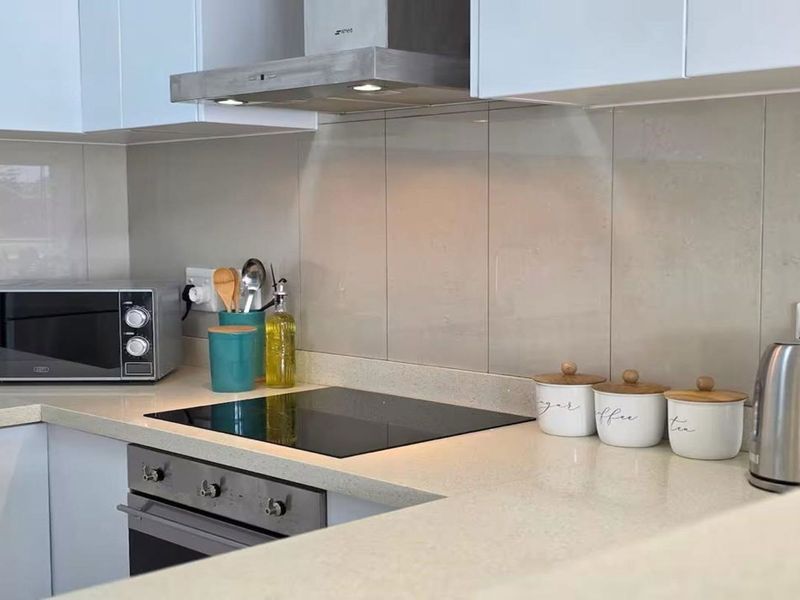 Modern kitchen featuring sleek white cabinetry, stone countertops, a glass electric hob, built-in oven, and a stainless steel extractor fan.
