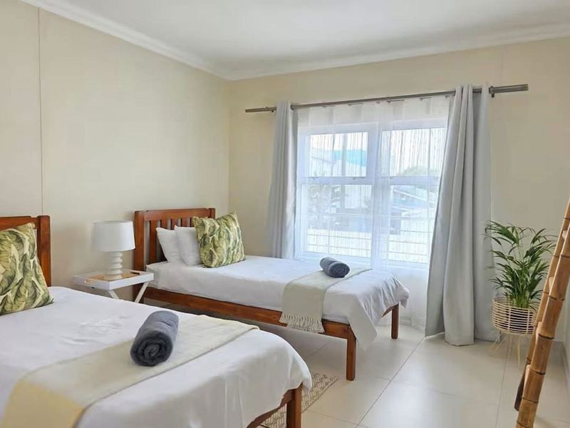 A bright and tidy bedroom featuring neutral wall tones, tiled flooring, and a large window with curtain rod installation.