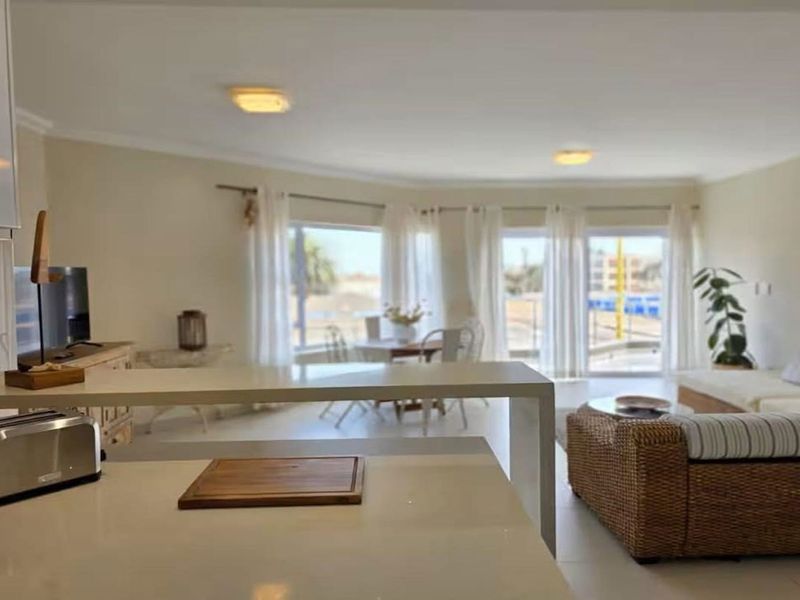 Bright open-plan living area featuring a modern kitchen island with stone countertops, flowing seamlessly into a spacious lounge with large sliding glass doors.