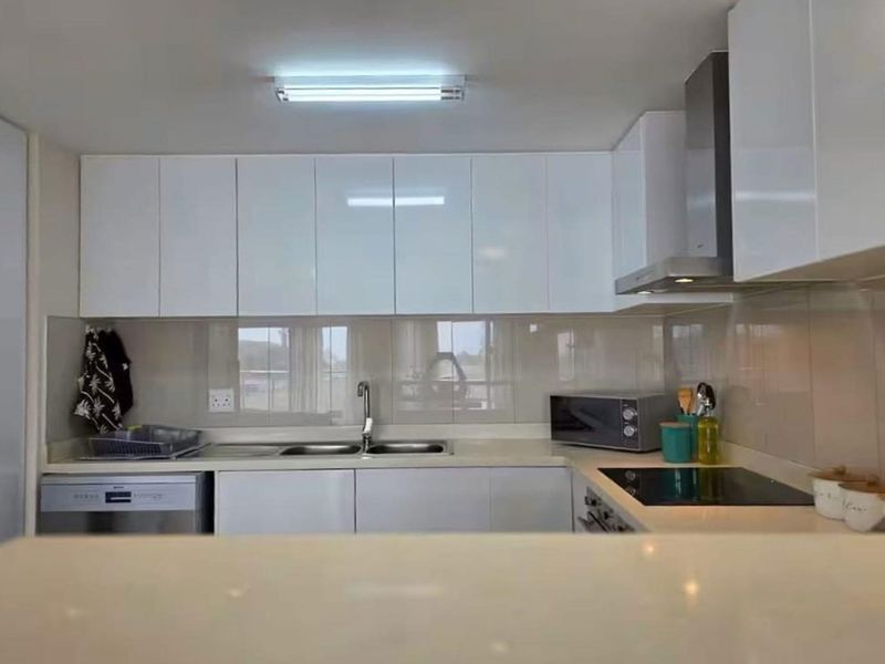 A modern kitchen featuring white gloss cabinetry, stone countertops, a stainless steel extractor fan, and an electric hob with a tiled splashback.