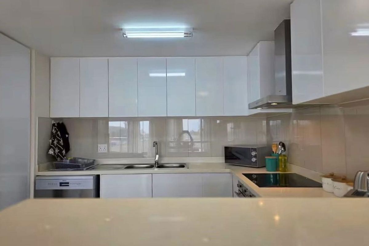 A modern kitchen featuring white gloss cabinetry, stone countertops, a stainless steel extractor fan, and an electric hob with a tiled splashback.