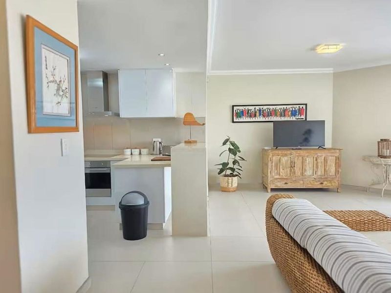 An open-plan living and kitchen area featuring tiled flooring, modern cabinetry, and integrated kitchen appliances in a bright, neutral setting.