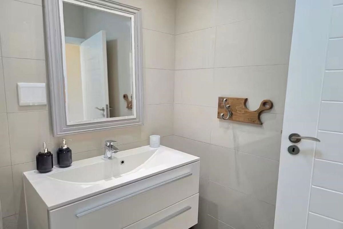 A modern bathroom featuring a sleek white vanity cabinet with a ceramic basin, chrome mixer tap, and a framed wall-mounted mirror.