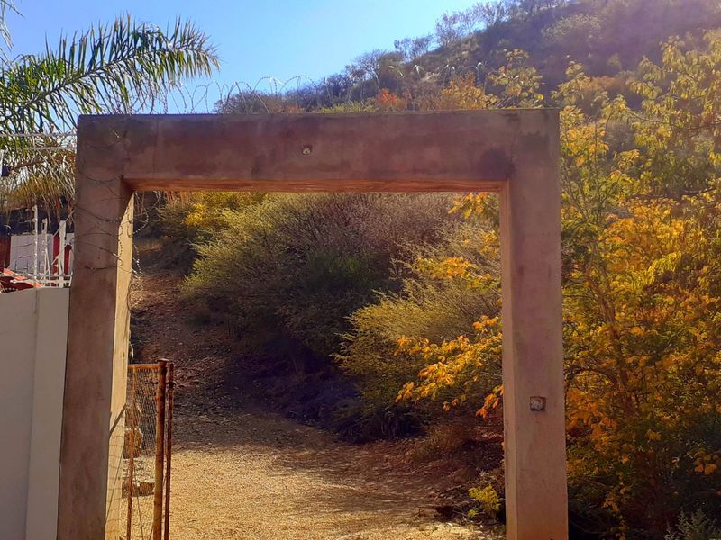 A concrete gate frame entrance leading to a sloped, natural landscape with surrounding metal fencing and razor wire security.