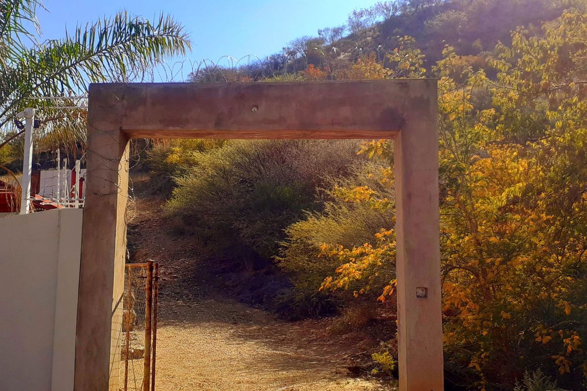 A concrete gate frame entrance leading to a sloped, natural landscape with surrounding metal fencing and razor wire security.
