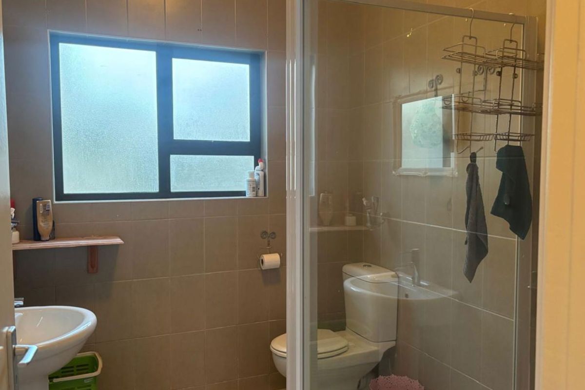 A functional bathroom featuring a pedestal basin, a glass-enclosed shower, and tiled walls, providing a practical layout for a townhouse residence.
