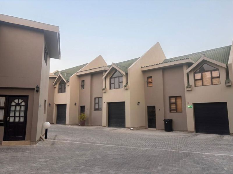 A view of the townhouse complex exterior featuring paved driveway access, multiple roller garage doors, and modern pitched roof architecture.