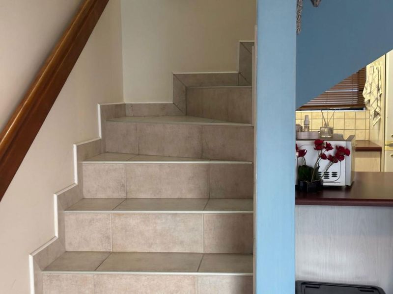 A staircase featuring tiled steps and a wooden handrail, providing access to the upper level of the townhouse.