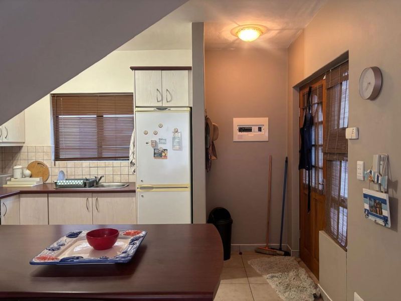 A functional kitchen area featuring built-in cabinetry, laminate countertops, and a tiled backsplash, adjacent to a side entrance door.