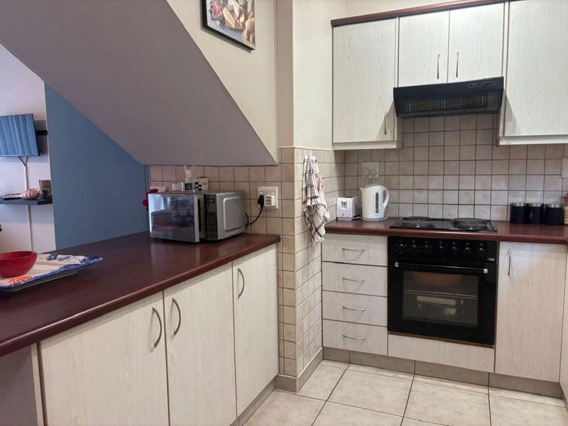 A functional kitchen featuring light wood-grain cabinetry, dark laminate countertops, a built-in oven with hob, and a tiled backsplash.