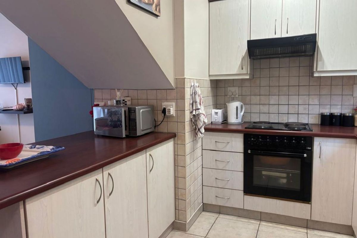 A functional kitchen featuring light wood-grain cabinetry, dark laminate countertops, a built-in oven with hob, and a tiled backsplash.