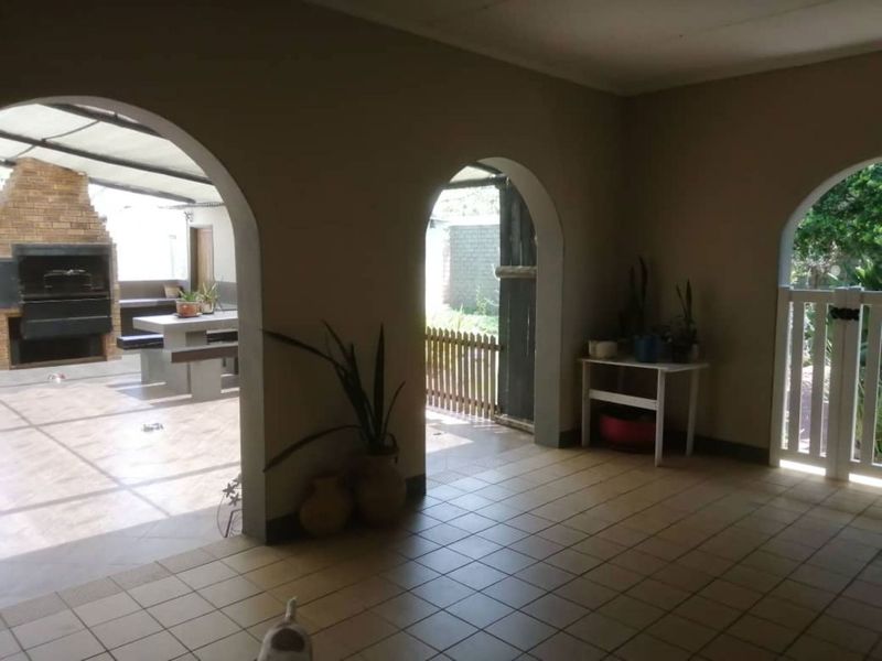 Covered patio area featuring arched doorways, tiled flooring, and a built-in braai, providing a seamless transition to the outdoor garden space.